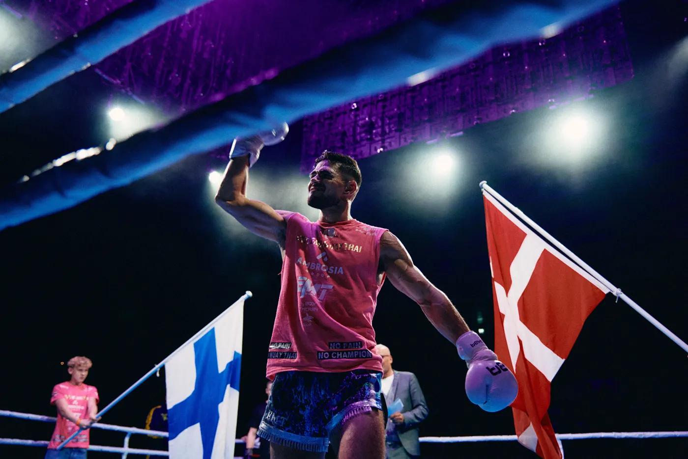 A fighter stands in the ring with an arm raised, a Finnish flag on one side of him and a Danish flag on the other
